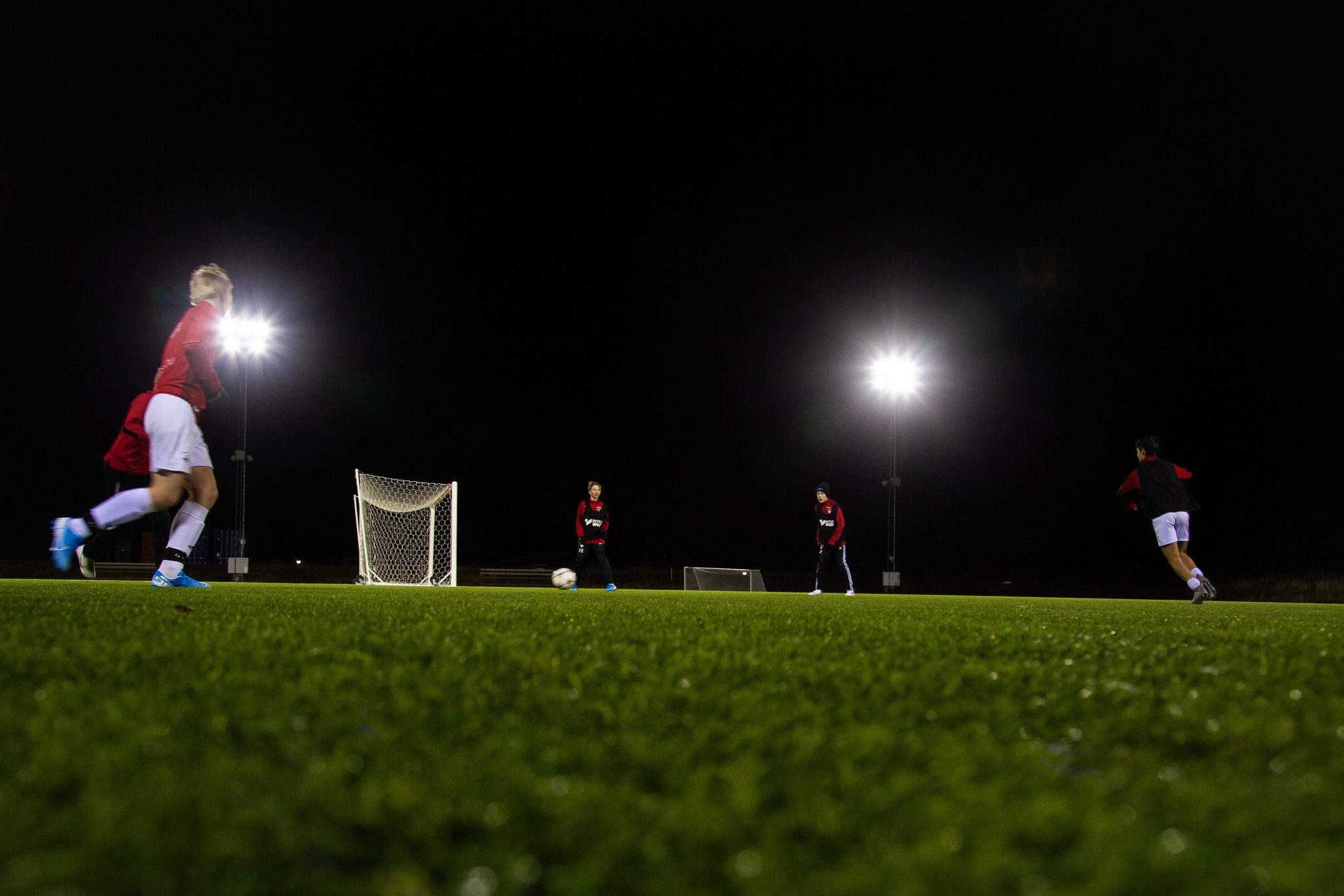 Ungdomar tränar fotboll en mörk kväll.