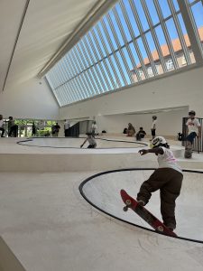 Ungdomar åker skateboard i vita t-shirts i luftig lokal med stoa takfönster.